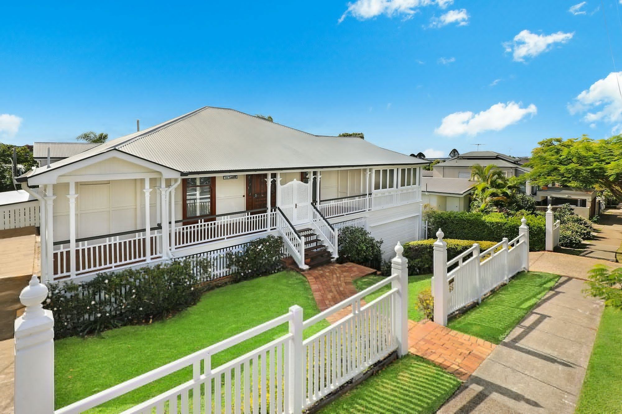 Queenslander style home with a white picket fence and green lawn